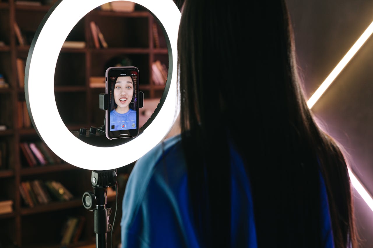 A woman records a video using a smartphone and ring light, perfect for content creators.